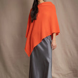 a woman wears a cashmere cape in orange with matching cashmere beanie hat over grey silk skirt