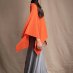 a woman wears a cashmere cape in orange with matching cashmere beanie hat over grey silk skirt