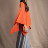 a woman wears a cashmere cape in orange with matching cashmere beanie hat over grey silk skirt