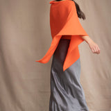 a woman wears a cashmere cape in orange with matching cashmere beanie hat over grey silk skirt