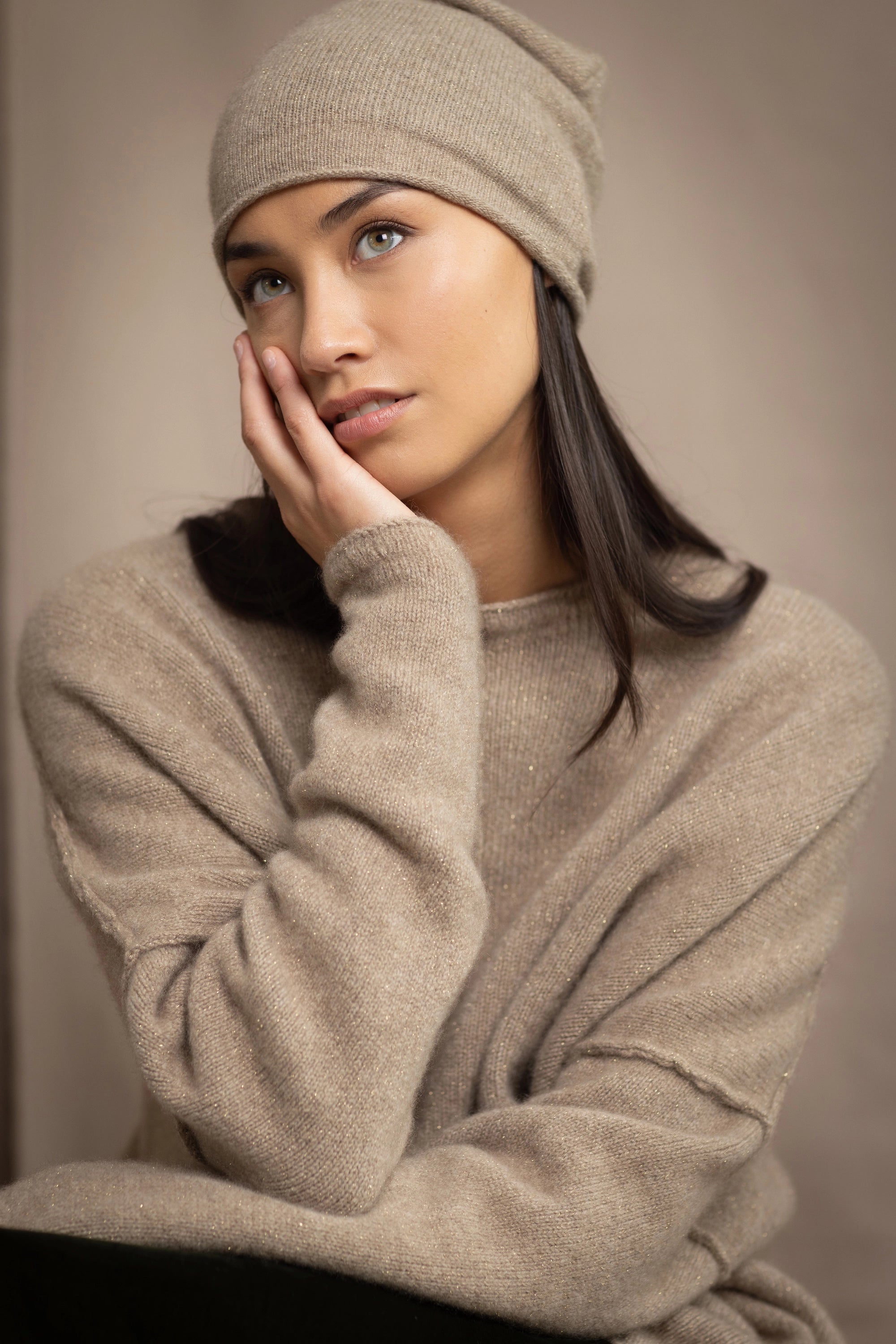 a woman wearing an oversized cashmere sweater in beige with gold metallic lurex thread and matching cashmere beanie hat