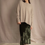 a woman wearing an oversized cashmere sweater in beige with gold metallic lurex thread and matching cashmere beanie hat over a silk velvet skirt in green