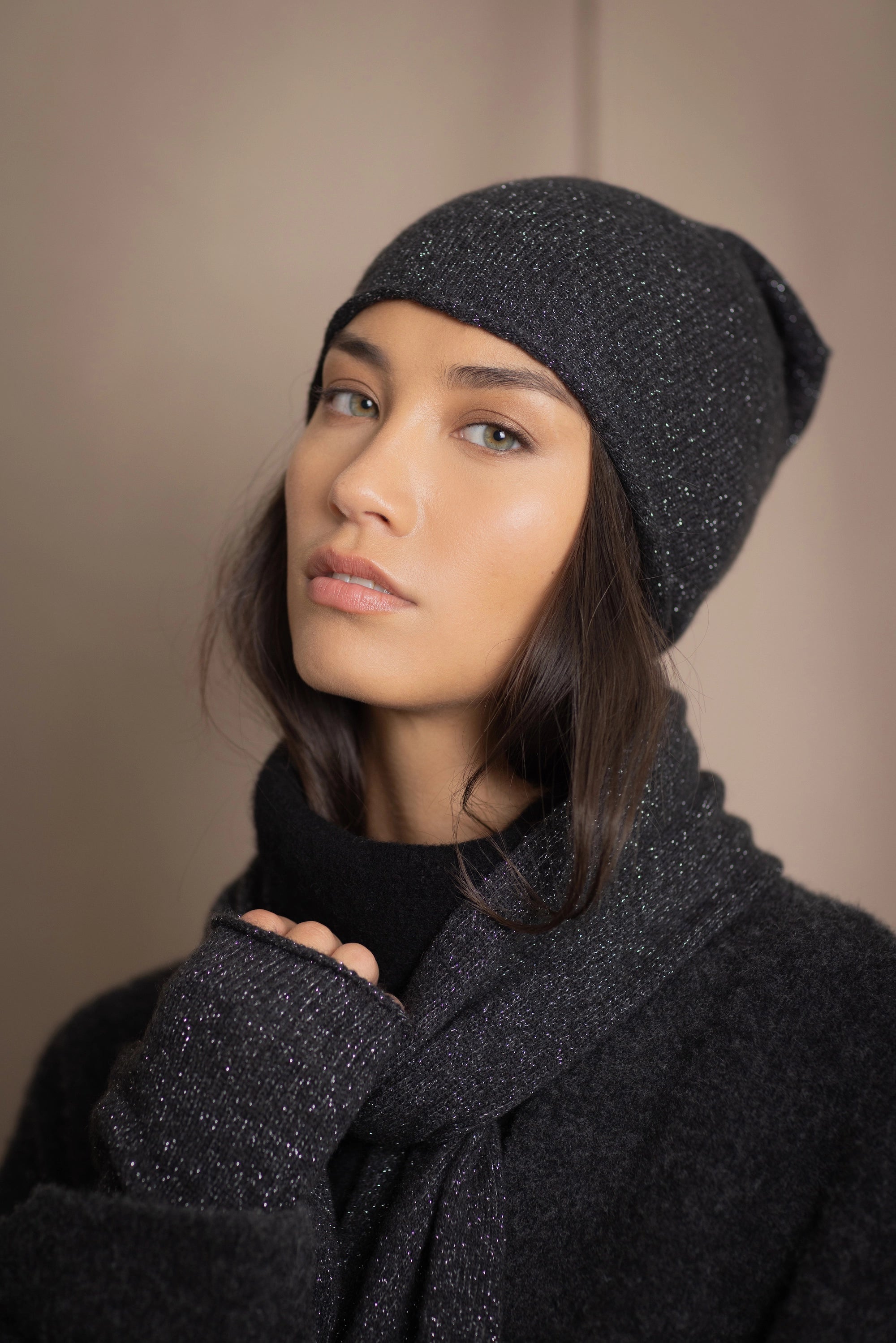 a woman wearing cashmere fingerless gloves and matching cashmere beanie hat in black with a metallic silver lurex thread through them