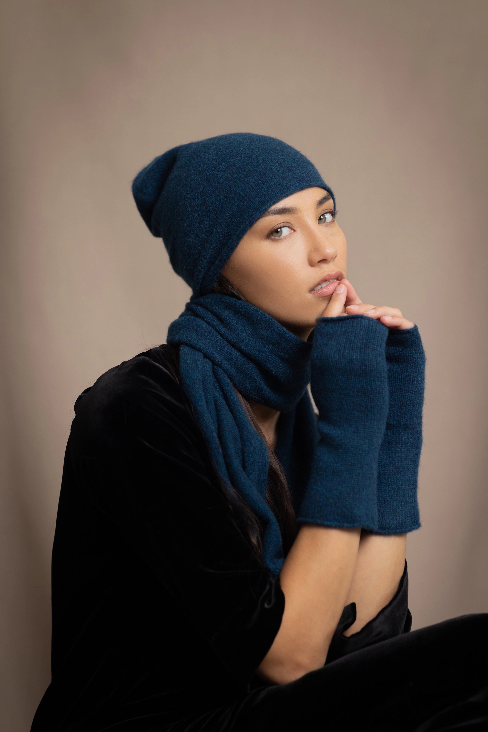 a woman wearing cashmere fingerless gloves in teal with cashmere beanie hat and small cashmere scarf in teal over silk velvet top in black