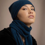 a woman wearing a cashmere scarf in teal with a cashmere beanie hat over black silk velvet clothing