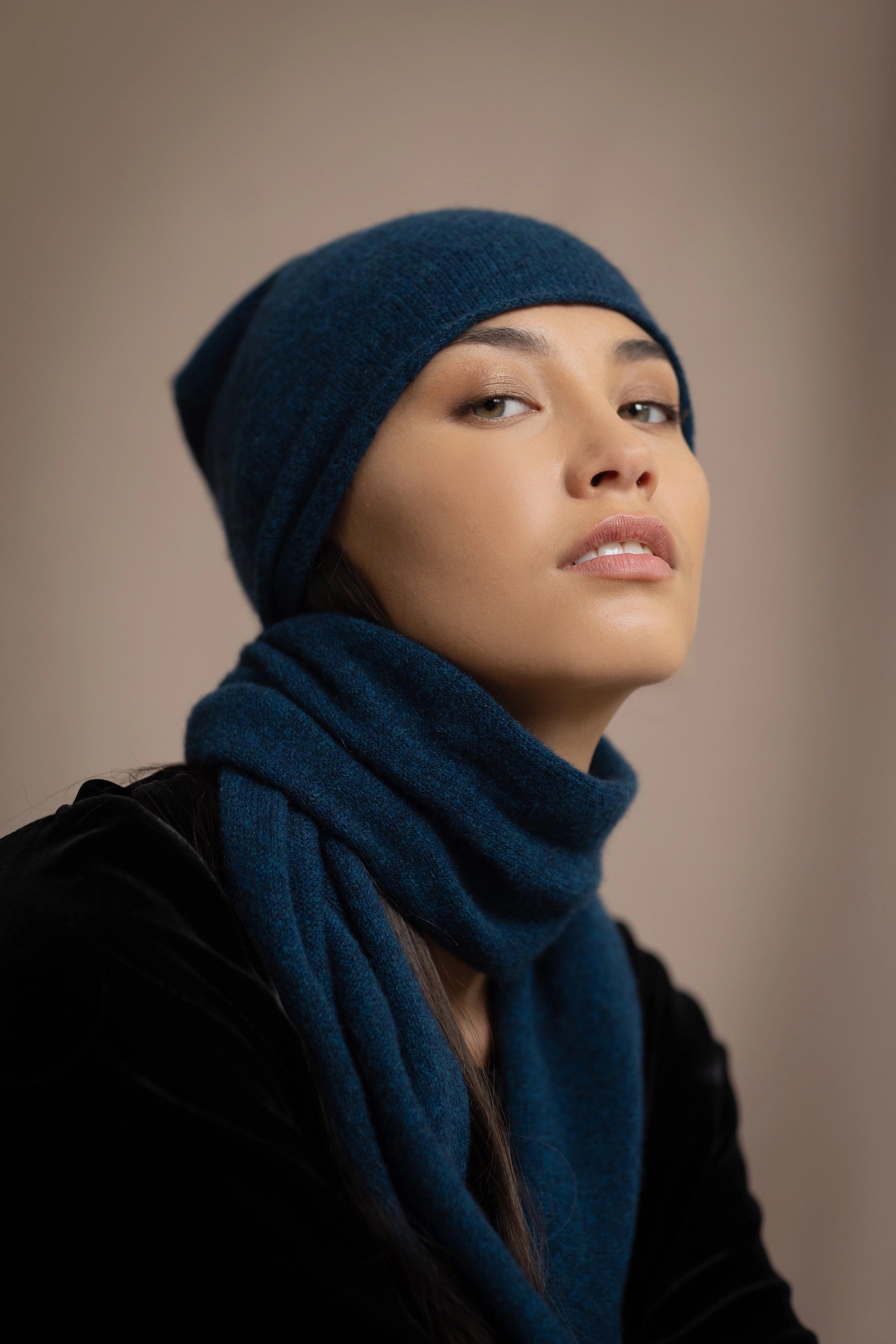 a woman wearing a cashmere scarf in teal with a cashmere beanie hat over black silk velvet clothing