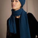 a woman wearing a cashmere scarf in teal with a cashmere beanie hat over black silk velvet clothing
