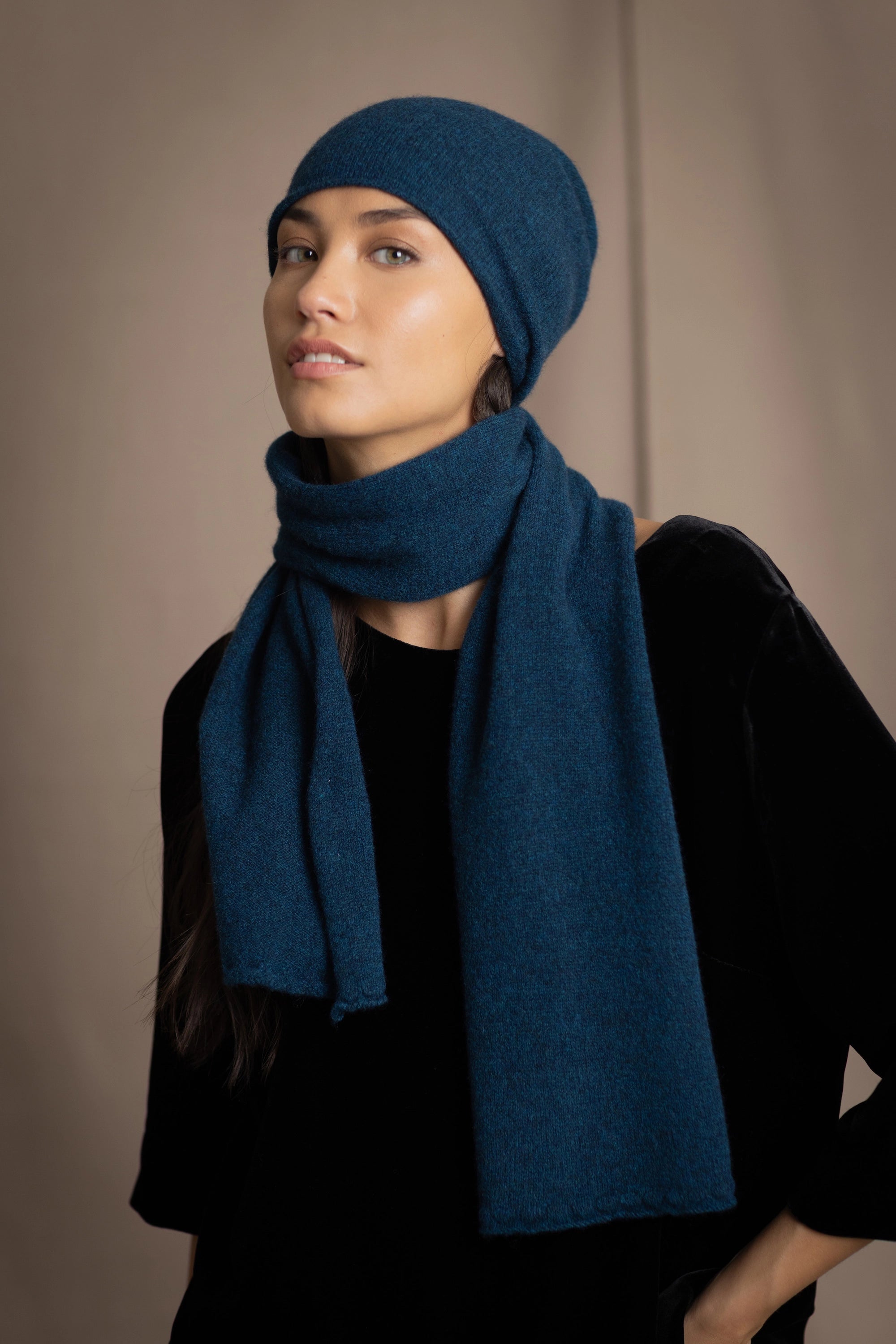 a woman wearing a cashmere scarf in teal with a cashmere beanie hat over black silk velvet clothing