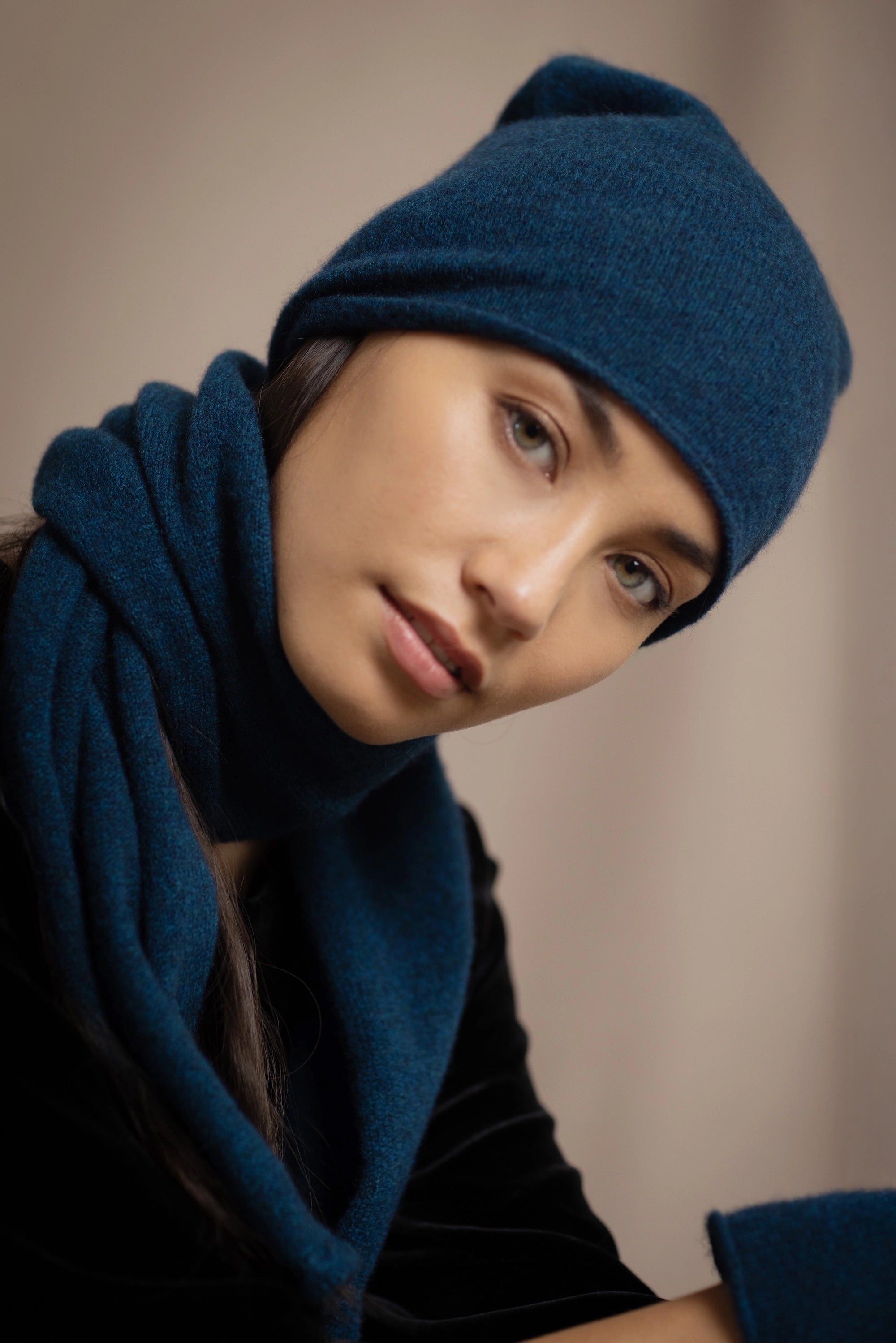 a woman wearing a cashmere scarf in teal with a cashmere beanie hat over black silk velvet clothing