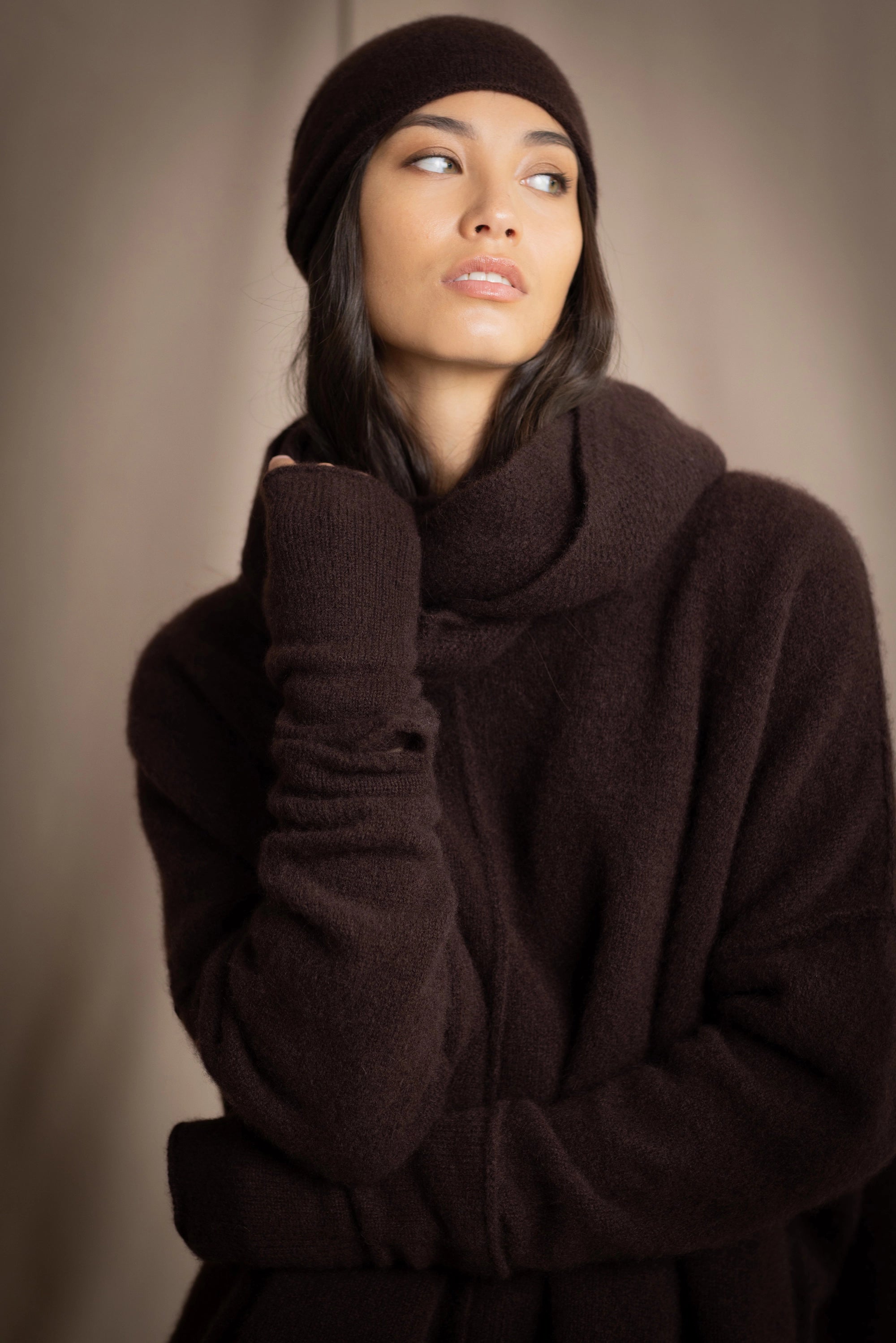 a woman wearing cashmere fingerless gloves in dark brown with matching cashmere beanie hat and cashmere snood and cashmere sweater