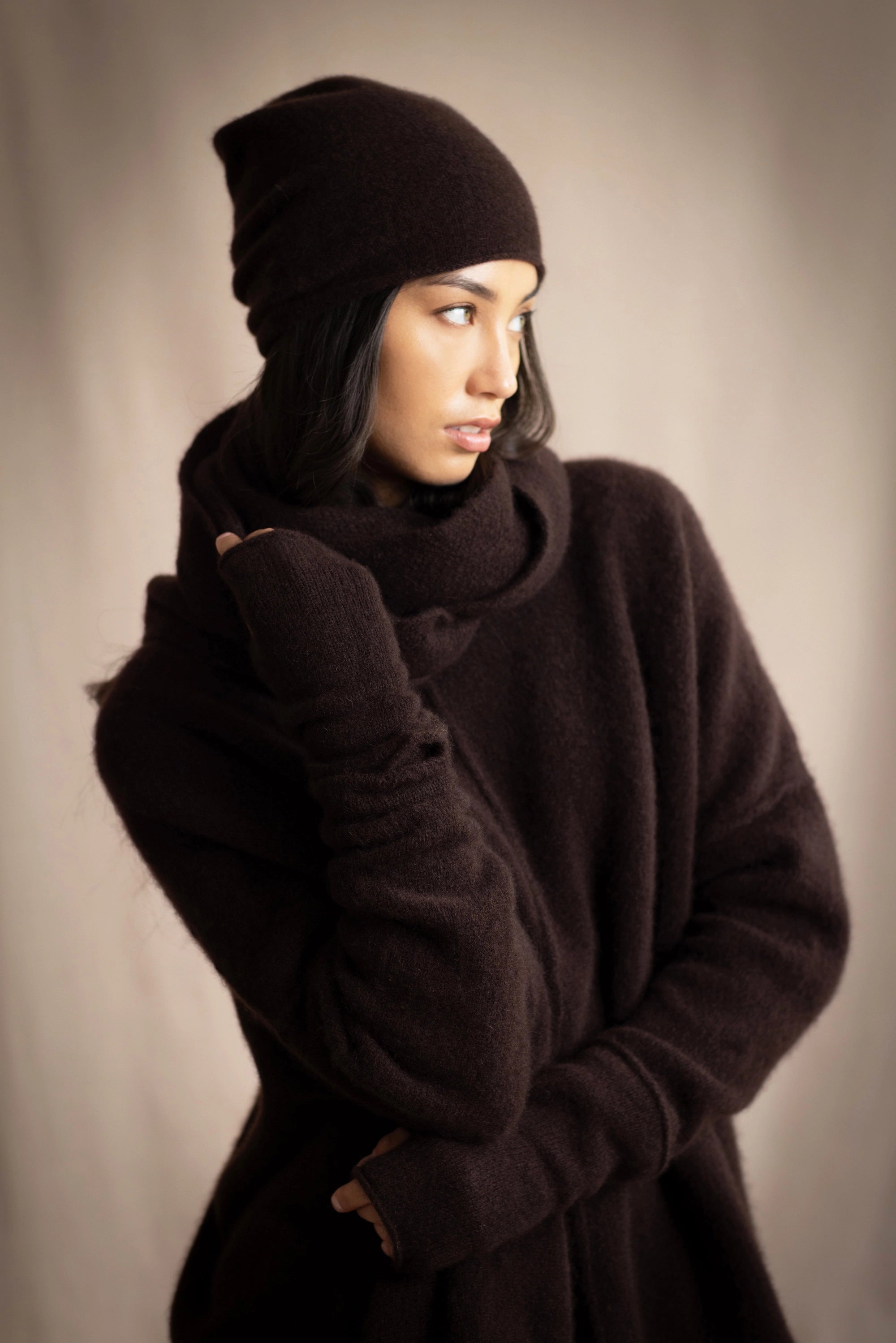 a woman wearing cashmere fingerless gloves in dark brown with matching cashmere beanie hat and cashmere snood and cashmere sweater
