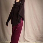 a woman wearing an oversized cashmere sweater in dark brown with matching cashmere beanie hat, snood and fingerless gloves over silk trousers in burgundy