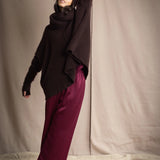a woman wearing an oversized cashmere sweater in dark brown with matching cashmere beanie hat, snood and fingerless gloves over silk trousers in burgundy