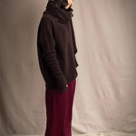 a woman wearing an oversized cashmere sweater in dark brown with matching cashmere beanie hat, snood and fingerless gloves over silk trousers in burgundy