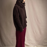 a woman wearing an oversized cashmere sweater in dark brown with matching cashmere beanie hat, snood and fingerless gloves over silk trousers in burgundy