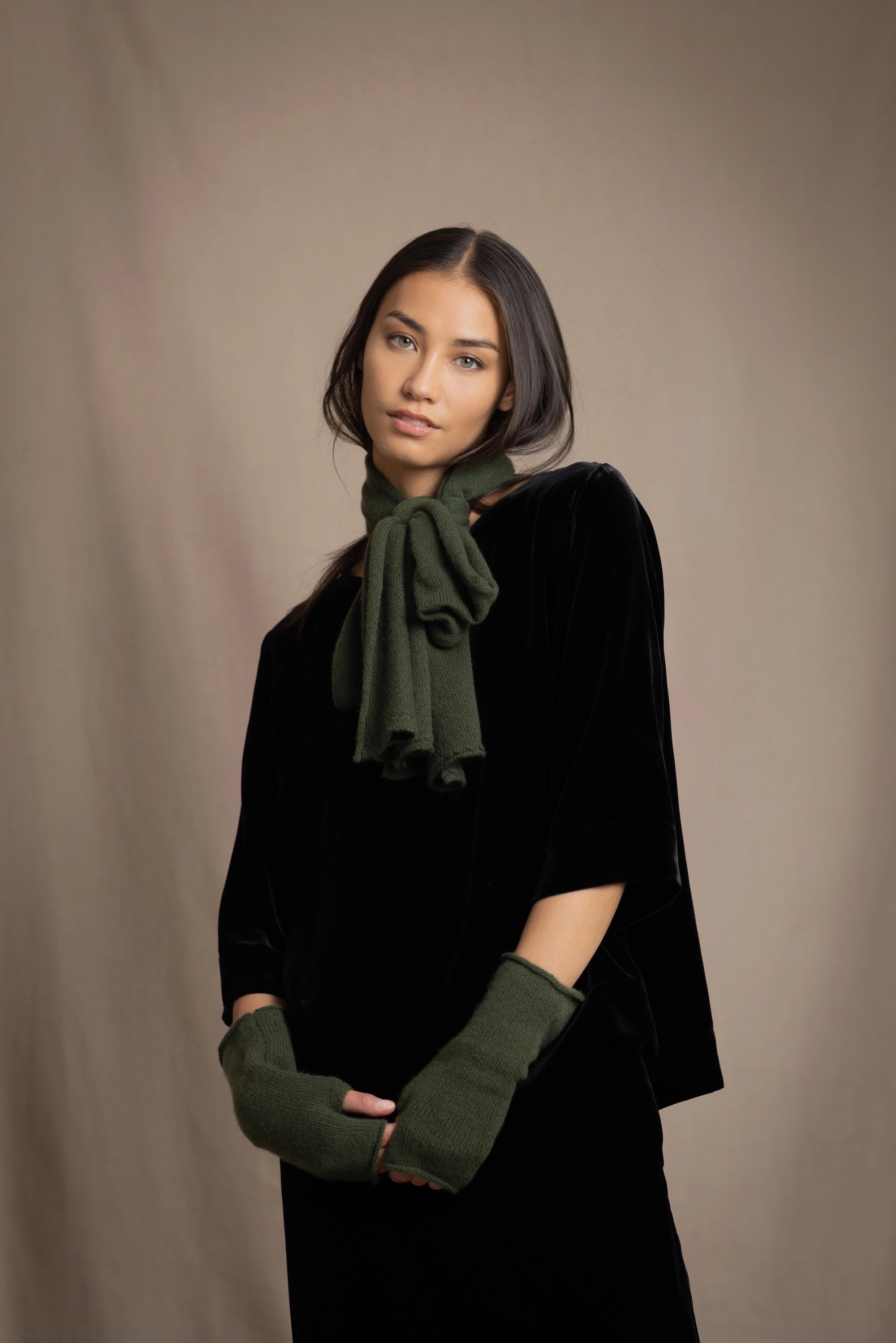 a woman wearing cashmere fingerless gloves in green and small cashmere scarf in green over silk velvet top in black