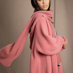 Woman wearing a long cashmere coat and matching scarf in dusty rose pink over a  pewter gray silk top and blue jeans
