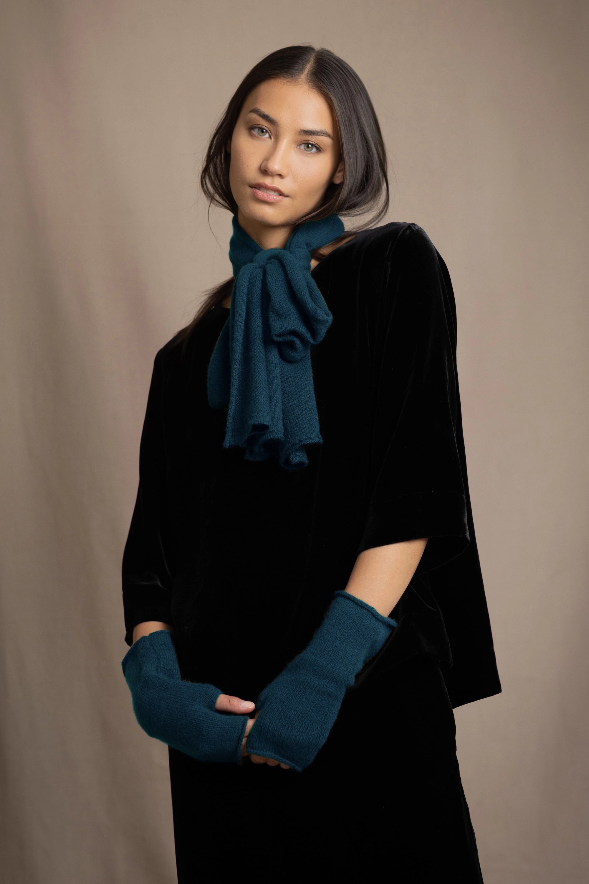a woman wearing a cashmere scarf in teal and fingerless cashmere gloves over black silk velvet top and trousers