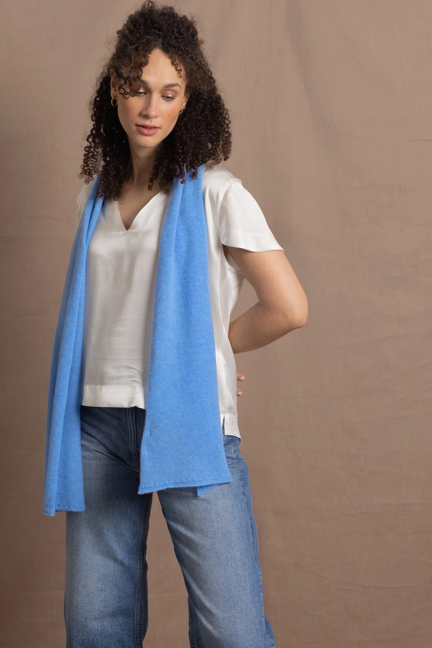 A woman wears a 100% silk v-neck t-shirt in white with a blue cashmere scarf and a pair of jeans
