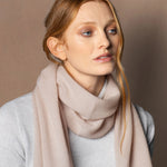 a lady wears a small cashmere scarf in a warm neutral beige colour