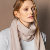 a lady wears a small cashmere scarf in a warm neutral beige colour