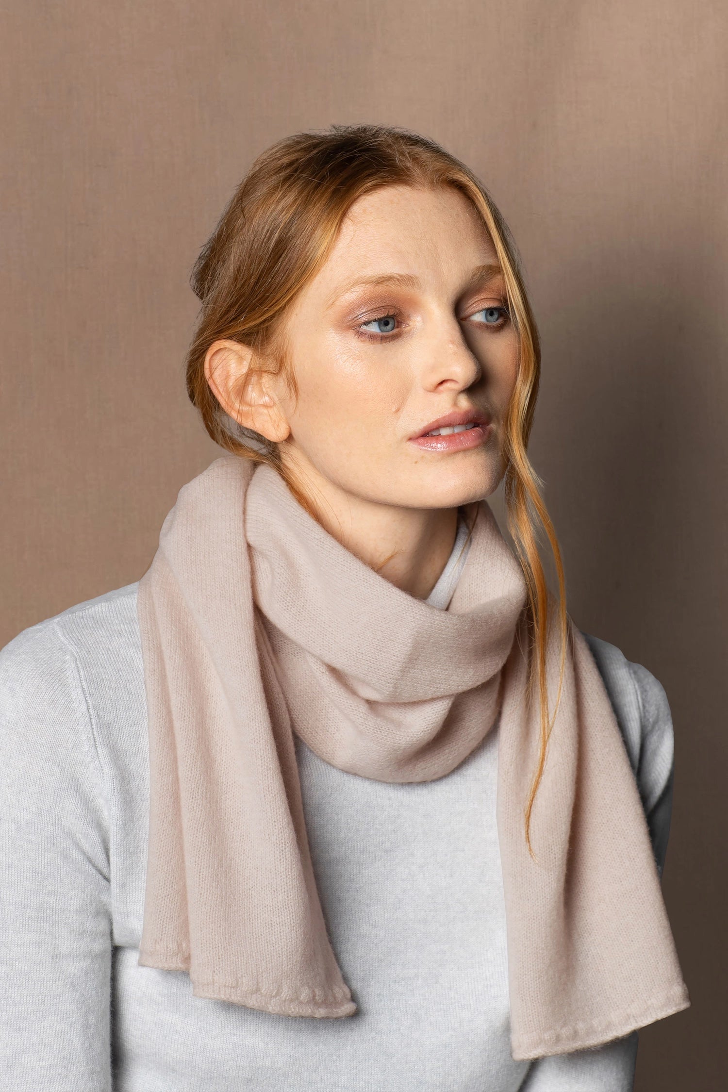 a lady wears a small cashmere scarf in a warm neutral beige colour
