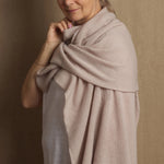 A woman wearing a beige cashmere wrap draped over her shoulders, providing a stylish and elegant look.