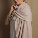 A woman wearing a beige cashmere wrap draped over her shoulders, providing a stylish and elegant look.