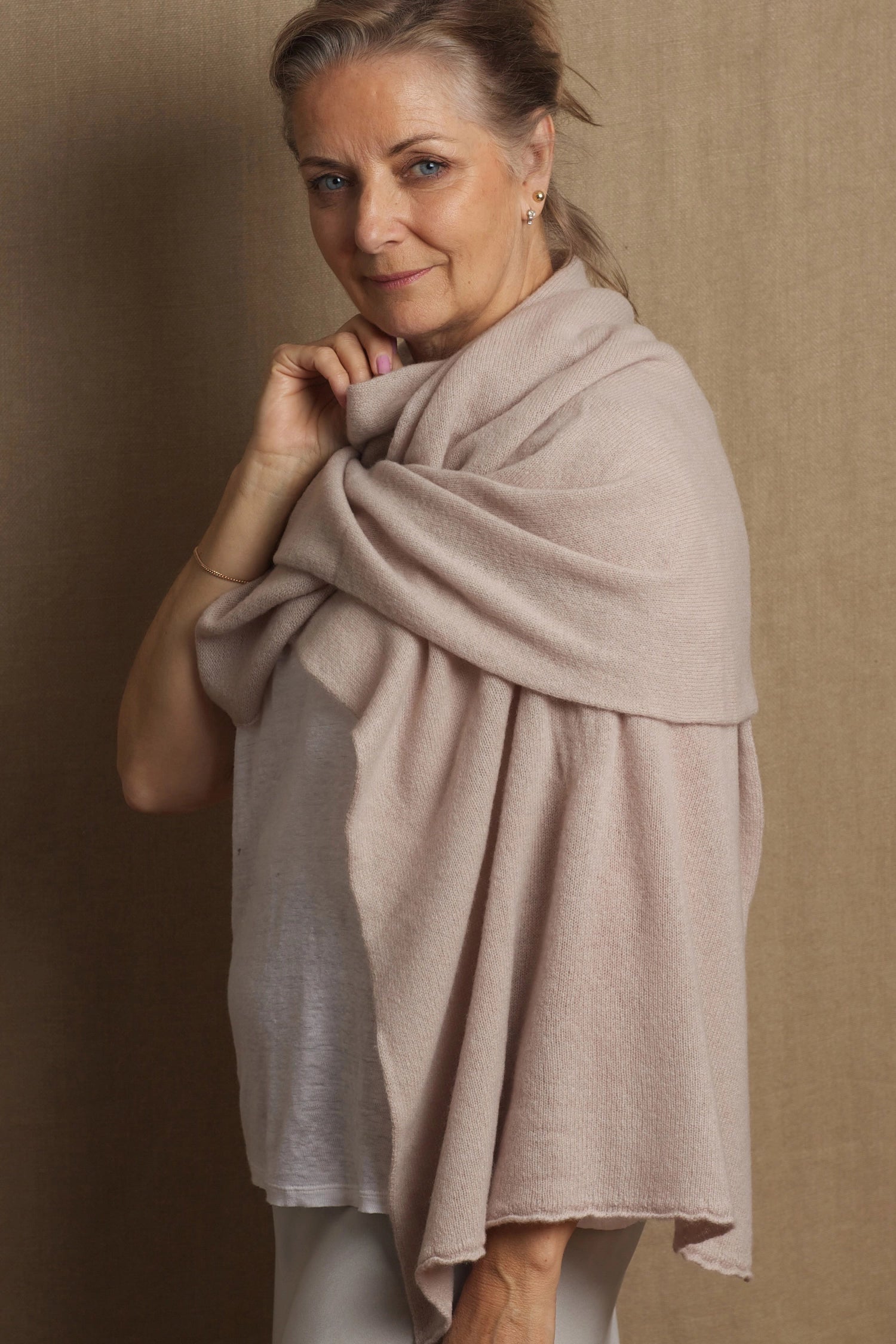 A woman wearing a beige cashmere wrap draped over her shoulders, providing a stylish and elegant look.
