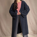 Woman wearing a long navy cashmere kaftan coat over a pink top and gray silk pants