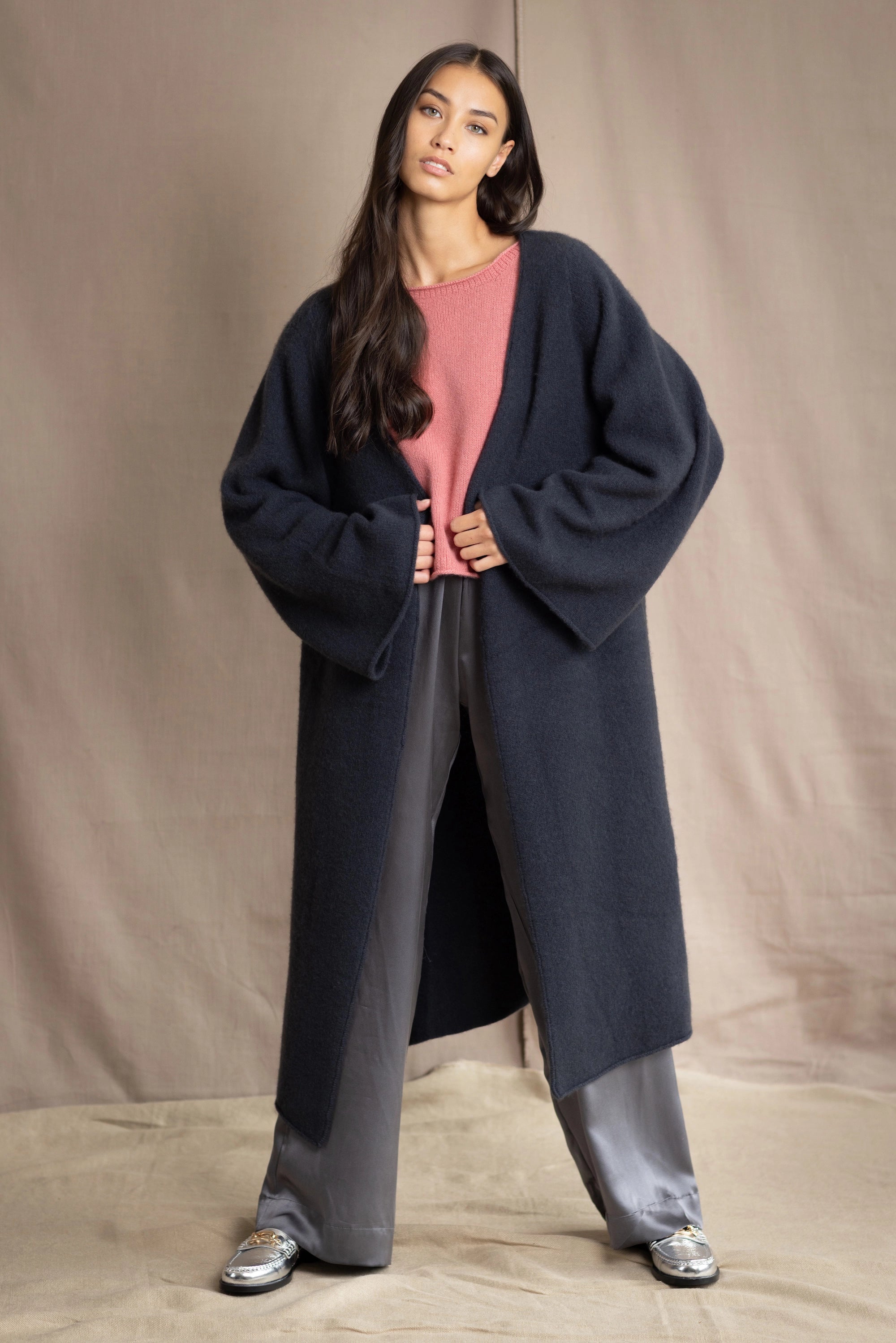 Woman wearing a long navy cashmere kaftan coat over a pink top and gray silk pants