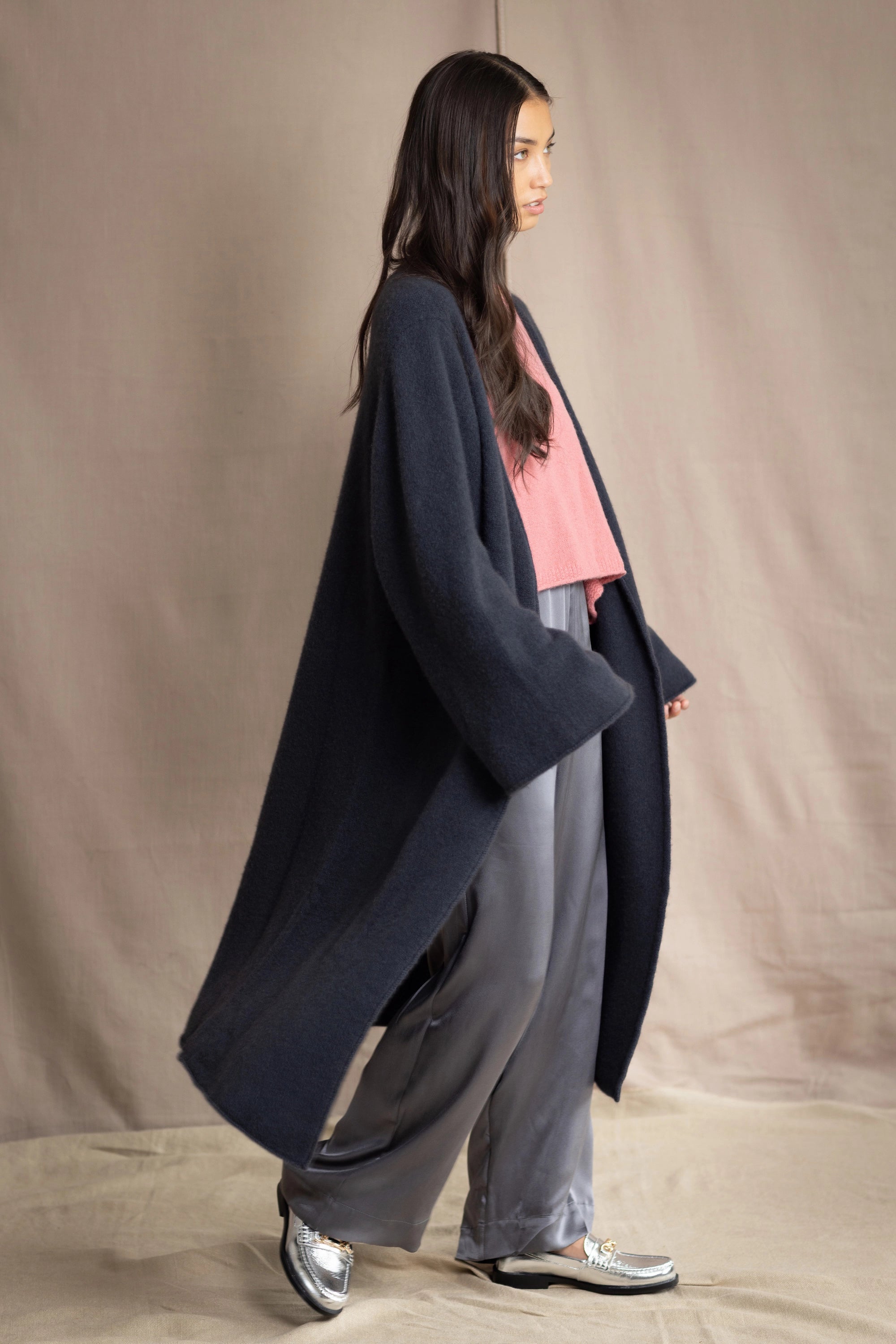 Woman wearing a long navy cashmere kaftan coat over a pink top and gray silk pants