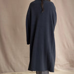 Woman wearing a long navy cashmere kaftan coat over a pink top and gray silk pants