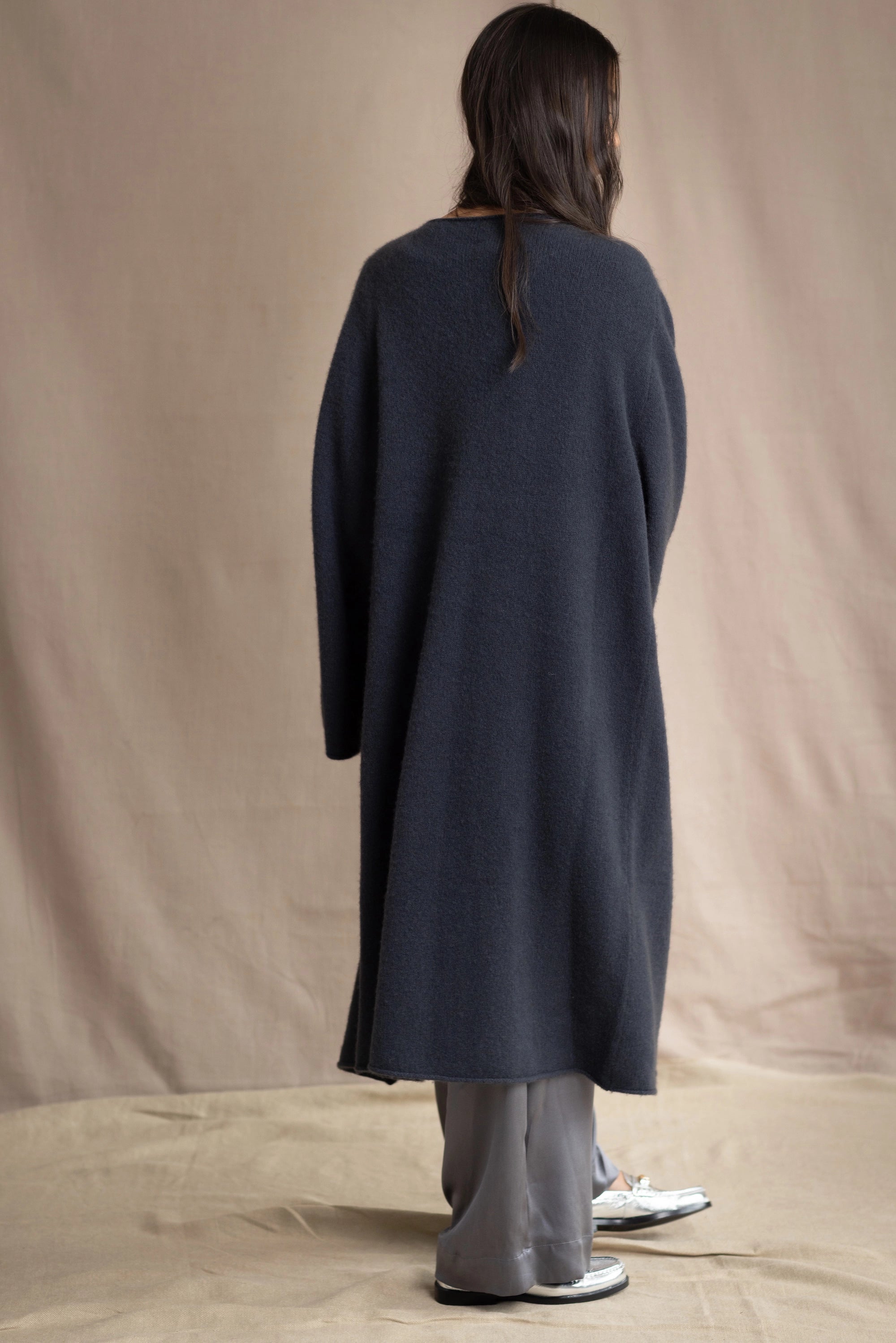 Woman wearing a long navy cashmere kaftan coat over a pink top and gray silk pants