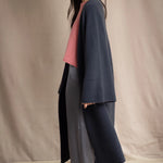 Woman wearing a long navy cashmere kaftan coat over a pink top and gray silk pants