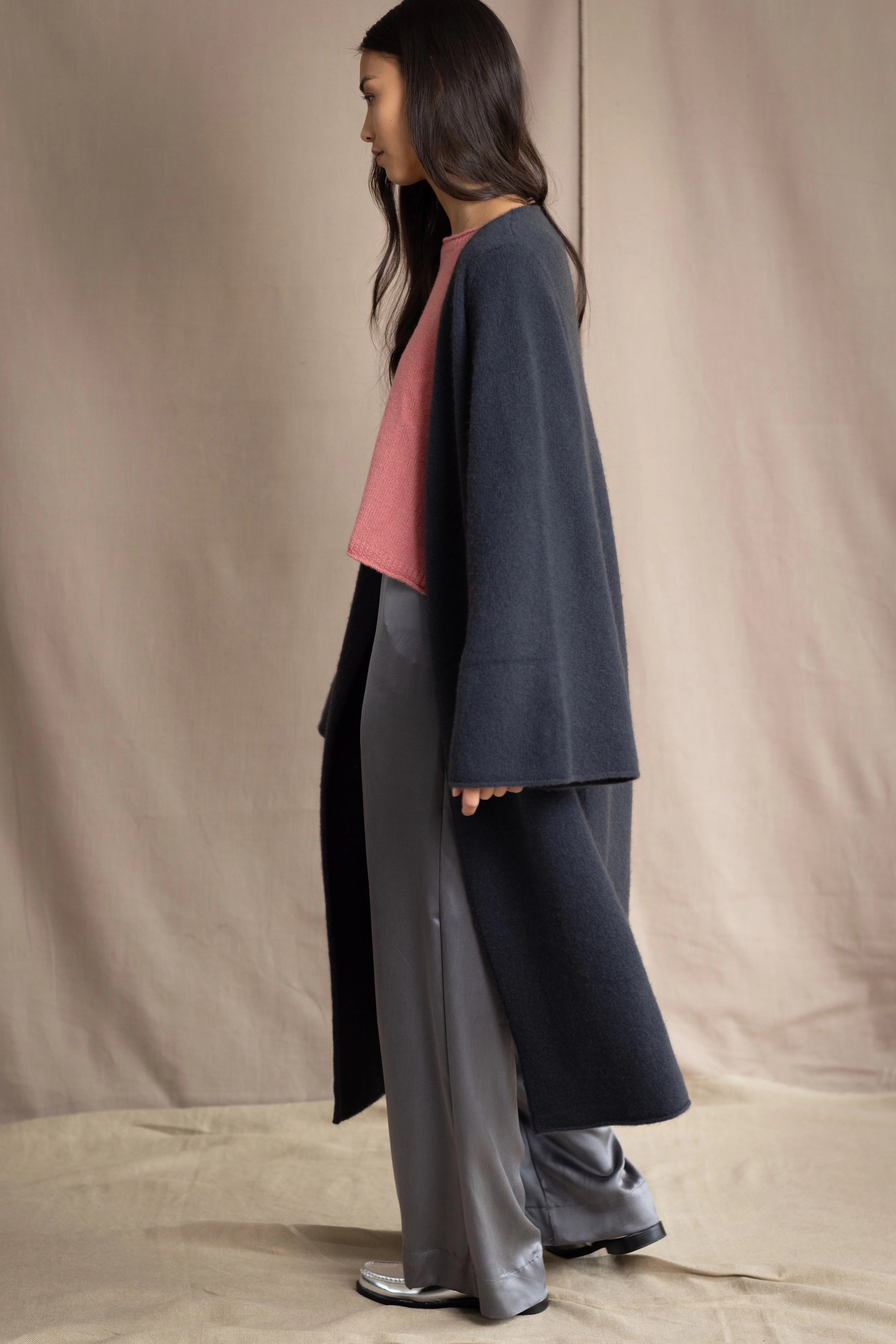 Woman wearing a long navy cashmere kaftan coat over a pink top and gray silk pants
