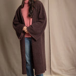 Woman wearing a long brown cashmere coat, pink cashmere sweater, blue jeans, and pink cashmere beanie