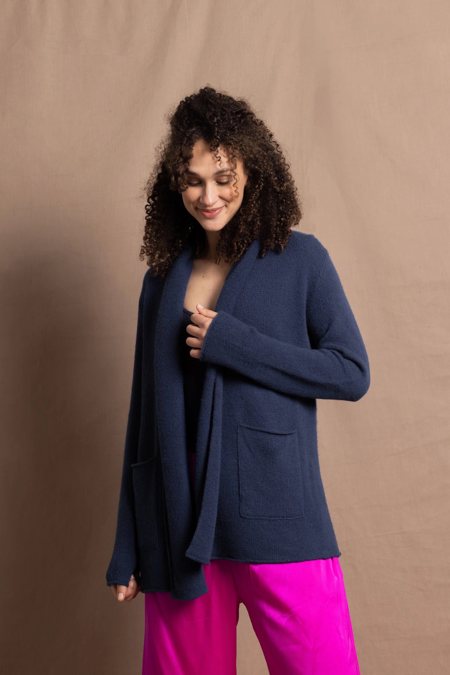 A woman wears a long cashmere cardigan in inky blue colour over bright pink silk trousers