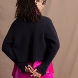 A woman wears a 100% cashmere cropped cardigan on top in navy blue over a 100% pure silk top in bright shocking pink over matching trousers