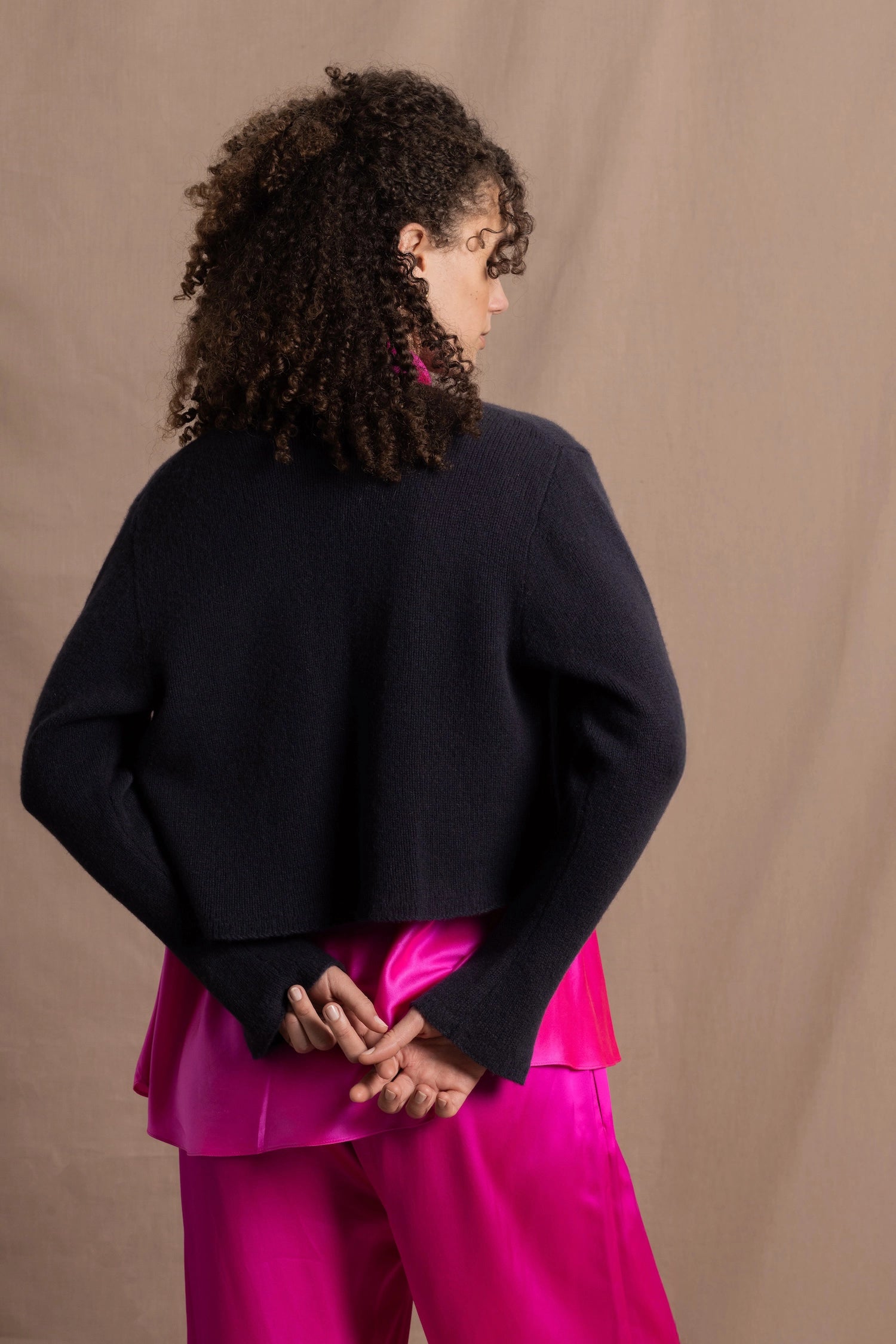 A woman wears a 100% cashmere cropped cardigan on top in navy blue over a 100% pure silk top in bright shocking pink over matching trousers