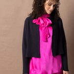 A woman wears a 100% cashmere cropped cardigan on top in navy blue over a 100% pure silk top in bright shocking pink over matching trousers