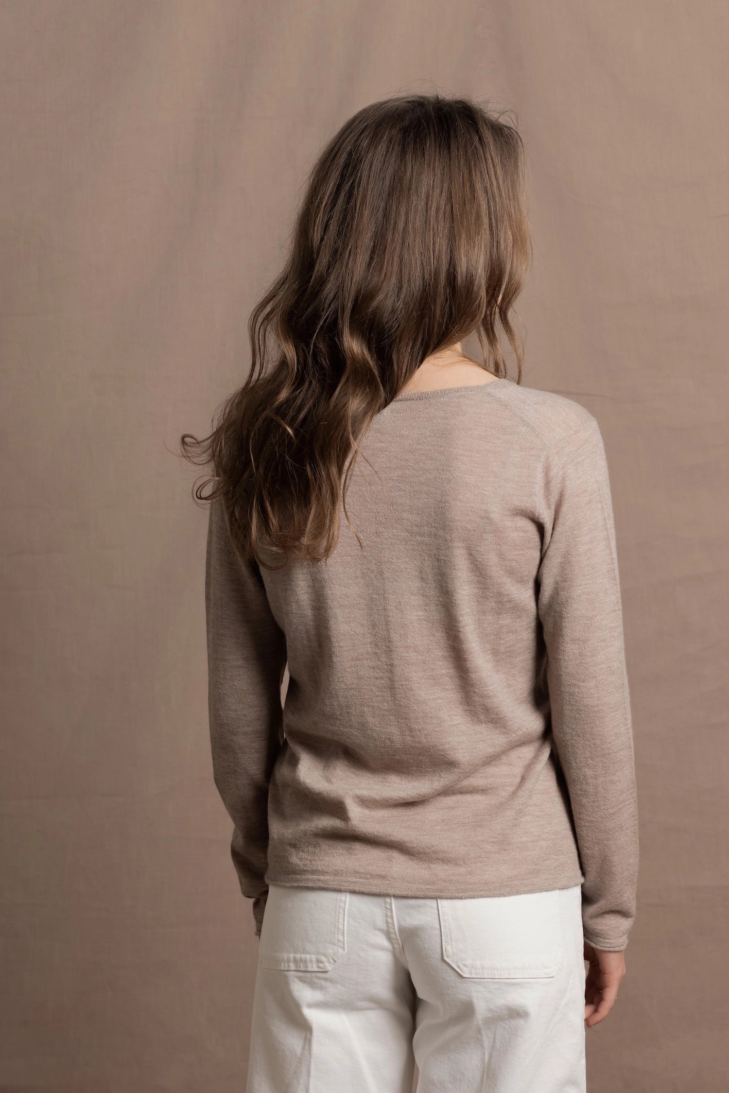 a woman wears a v neck thin summer weight cashmere sweater in a taupe colour and white jeans