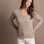 a woman wears a v neck thin summer weight cashmere sweater in a taupe colour and white jeans