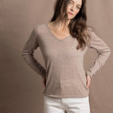 a woman wears a v neck thin summer weight cashmere sweater in a taupe colour and white jeans
