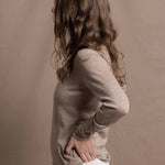 a woman wears a v neck thin summer weight cashmere sweater in a taupe colour and white jeans