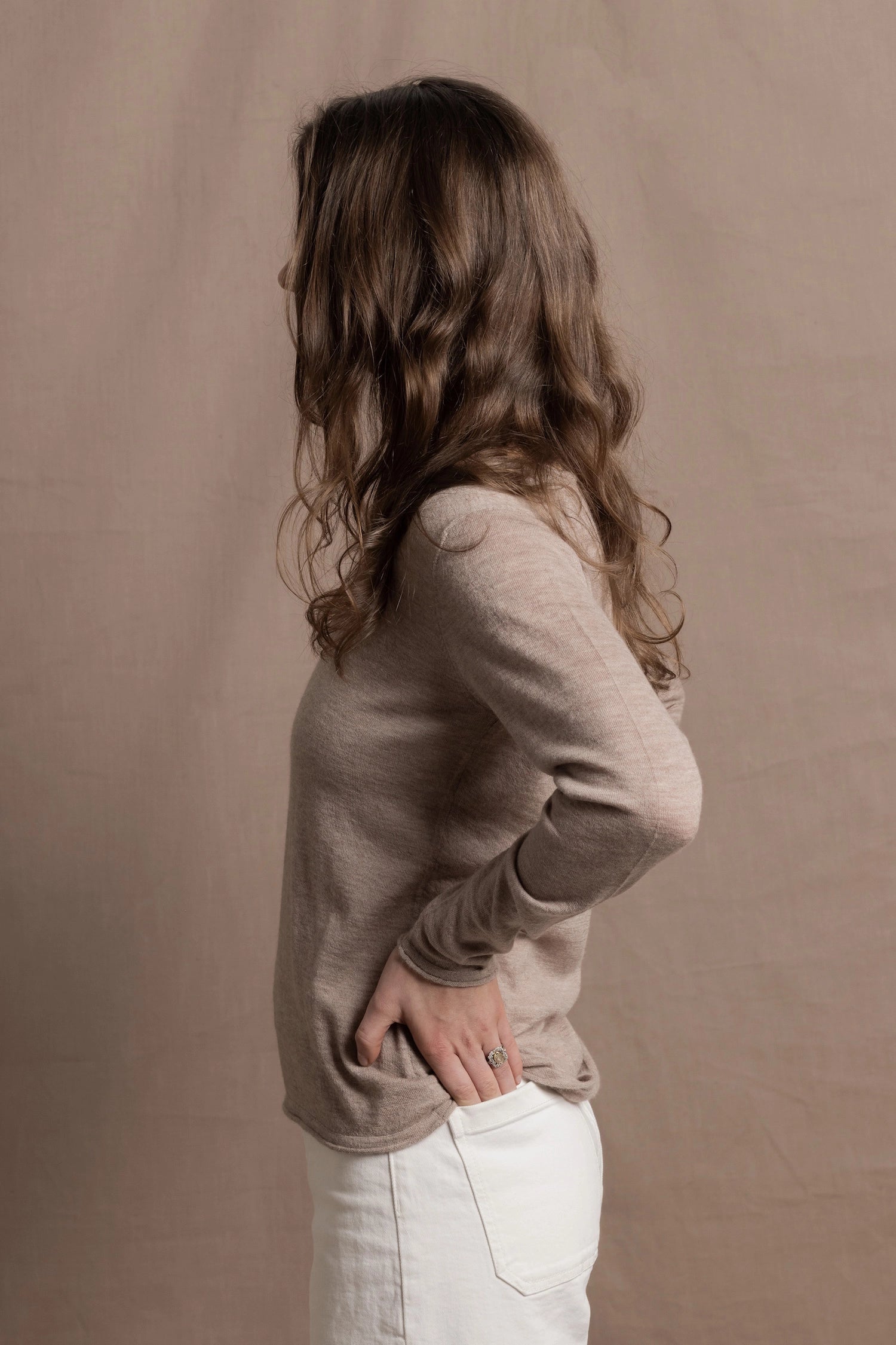 a woman wears a v neck thin summer weight cashmere sweater in a taupe colour and white jeans
