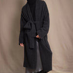 Woman wearing a long cashmere coat in dark grey over black cashmere turtleneck sweater and pewter silk skirt with black leather boots