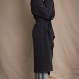 Woman wearing a long cashmere coat in dark grey over black cashmere turtleneck sweater and pewter silk skirt with black leather boots