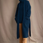 Woman wearing a long cashmere coat in teal blue over teal blue cashmere turtleneck sweater and bronze silk trousers