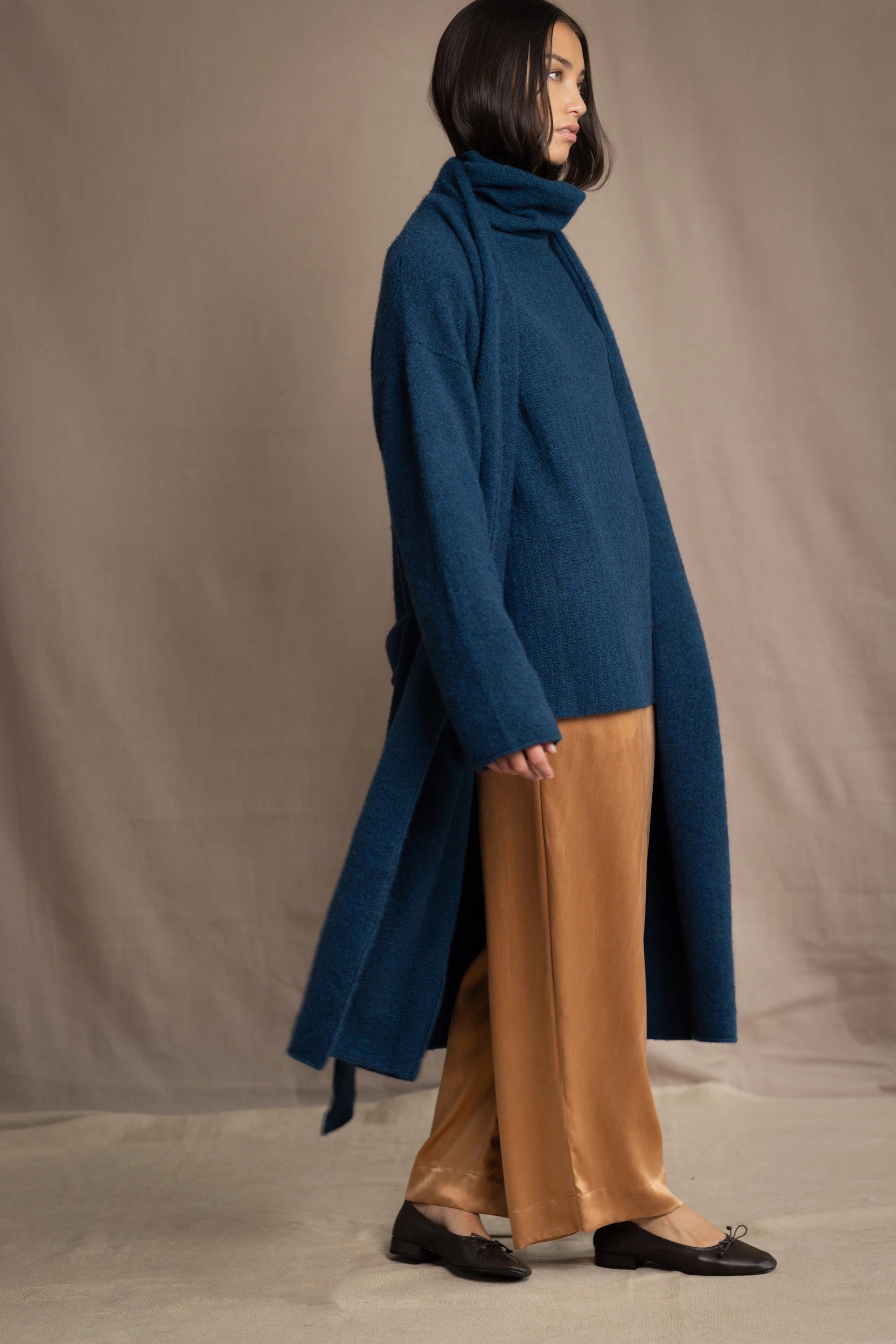 Woman wearing a long cashmere coat in teal blue over teal blue cashmere turtleneck sweater and bronze silk trousers